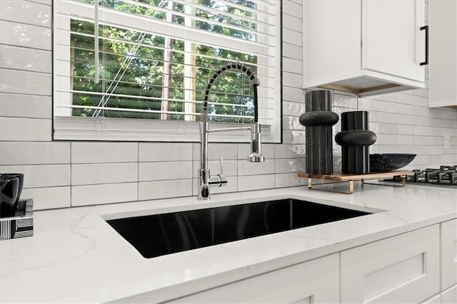 kitchen featuring light stone counters, white cabinetry, sink, and tasteful backsplash