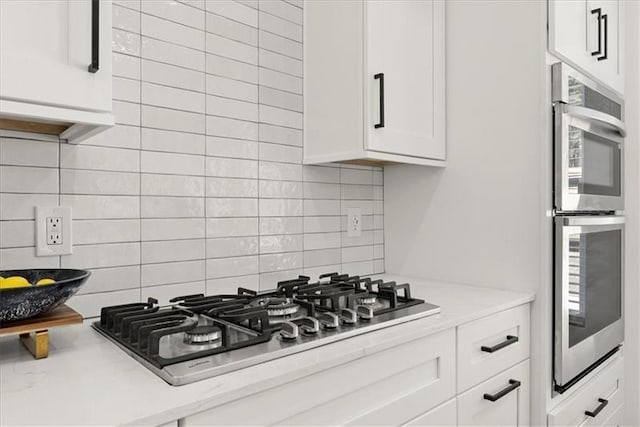 kitchen with backsplash, stainless steel appliances, white cabinetry, and light stone counters