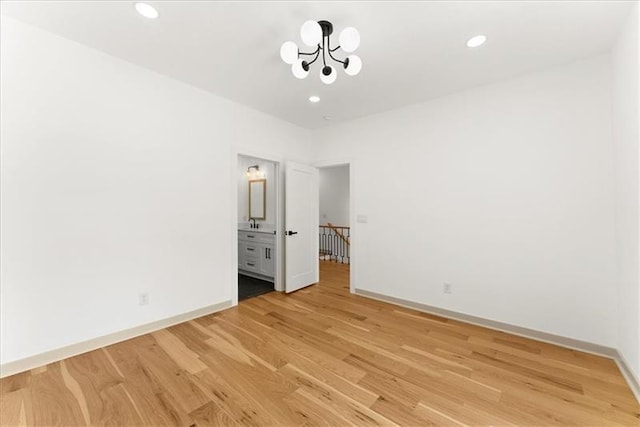 unfurnished bedroom featuring ensuite bath, an inviting chandelier, and light wood-type flooring