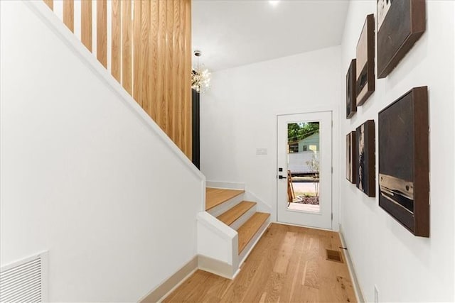 doorway to outside with light wood-type flooring and a notable chandelier