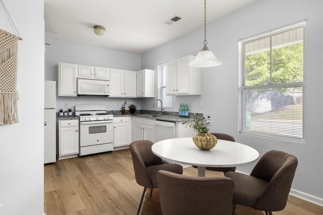 kitchen featuring white appliances, light wood-style flooring, white cabinets, and hanging light fixtures