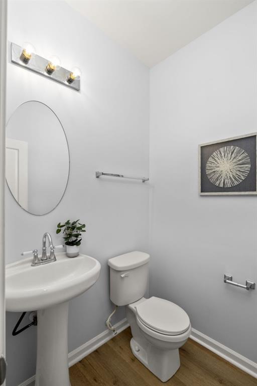 half bathroom featuring wood finished floors, toilet, and baseboards