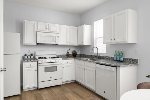 kitchen with white appliances, a sink, white cabinetry, wood finished floors, and dark stone countertops