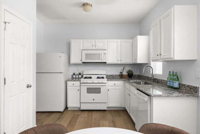 kitchen featuring white appliances, a sink, wood finished floors, white cabinets, and light stone countertops
