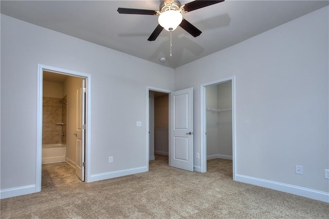 unfurnished bedroom featuring a spacious closet, a closet, connected bathroom, light colored carpet, and ceiling fan