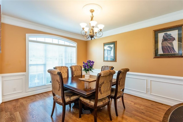 dining space with a healthy amount of sunlight, wood-type flooring, ornamental molding, and an inviting chandelier