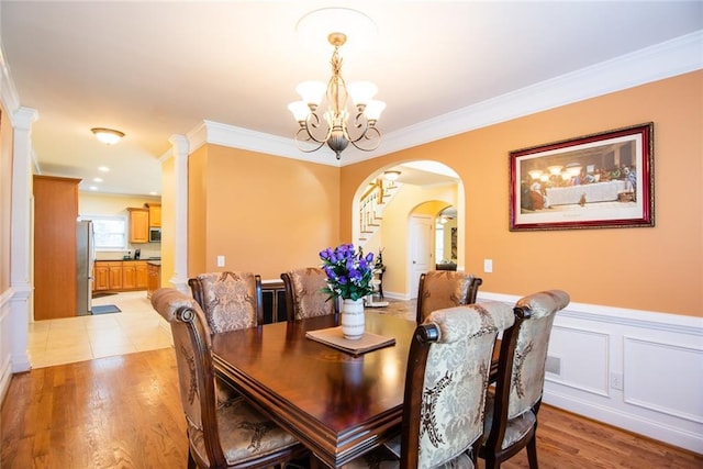 dining area featuring light hardwood / wood-style floors, ornamental molding, a chandelier, and ornate columns