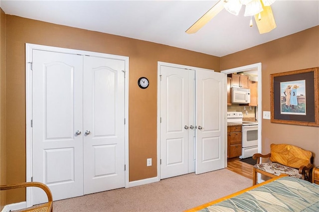 bedroom with baseboards, ceiling fan, two closets, and light colored carpet