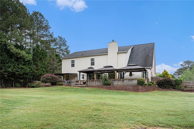 rear view of house featuring fence, a gazebo, a lawn, and a chimney