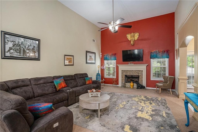 carpeted living room featuring a ceiling fan, arched walkways, a high ceiling, and a fireplace
