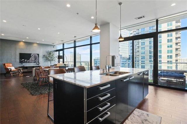 kitchen featuring visible vents, dark cabinets, a city view, floor to ceiling windows, and a sink