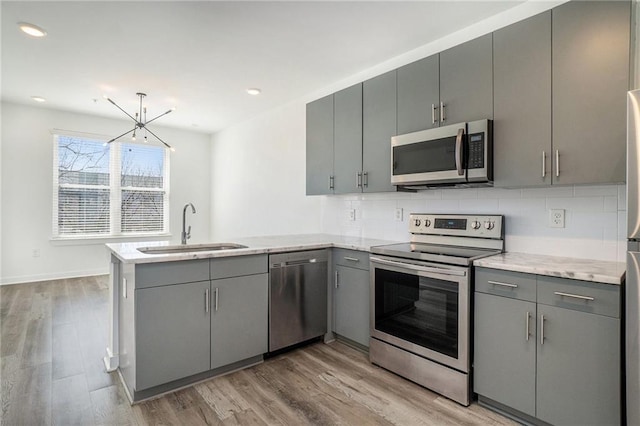 kitchen with a peninsula, gray cabinetry, appliances with stainless steel finishes, and a sink