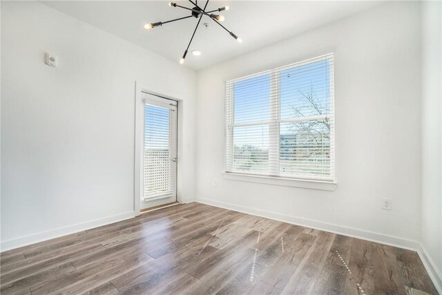 spare room with baseboards, wood finished floors, and a chandelier