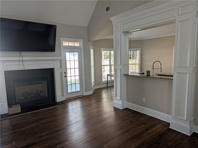 unfurnished living room with baseboards, visible vents, a fireplace with raised hearth, dark wood-style flooring, and vaulted ceiling