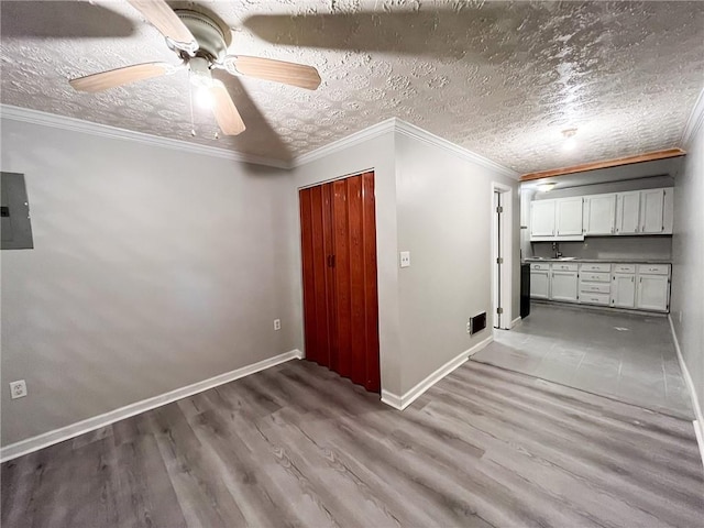 empty room featuring ceiling fan, electric panel, light wood-type flooring, a textured ceiling, and ornamental molding