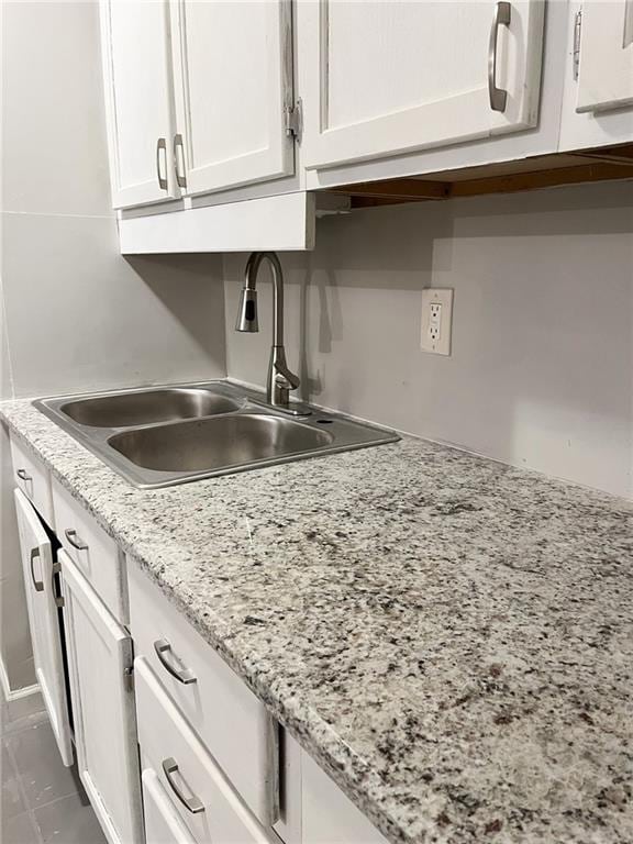 kitchen featuring white cabinets, light stone counters, dark tile patterned floors, and sink