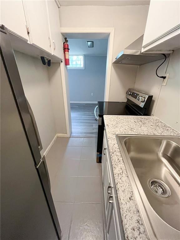 kitchen with light stone counters, sink, white cabinetry, stainless steel refrigerator, and light tile patterned flooring