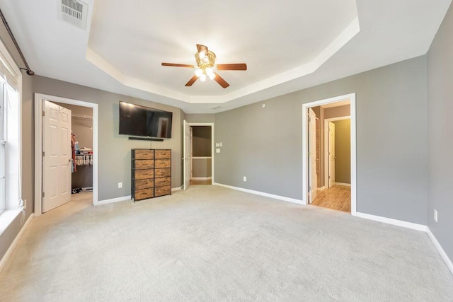 unfurnished bedroom with a spacious closet, ceiling fan, a raised ceiling, light colored carpet, and a closet