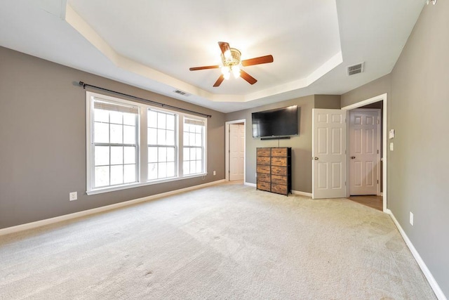 unfurnished bedroom featuring a tray ceiling, ceiling fan, and light colored carpet