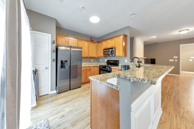 kitchen with sink, light hardwood / wood-style flooring, light stone counters, kitchen peninsula, and stainless steel appliances