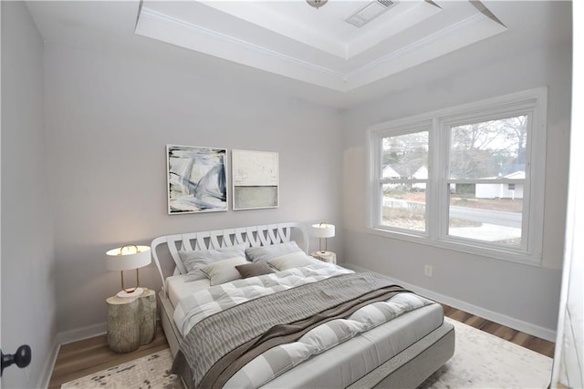 bedroom featuring wood-type flooring, a tray ceiling, and ornamental molding