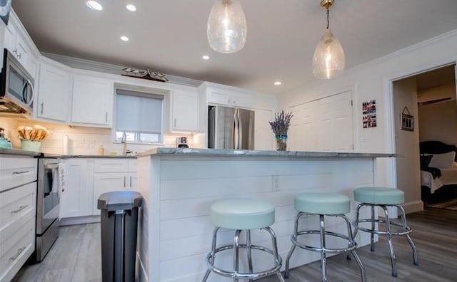 kitchen featuring pendant lighting, hardwood / wood-style floors, stainless steel appliances, white cabinets, and a kitchen bar