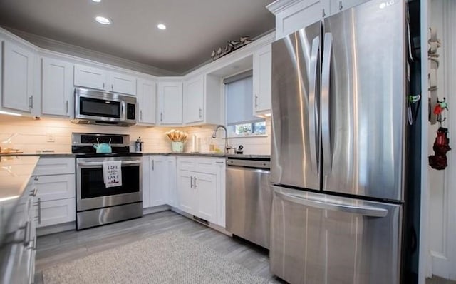 kitchen featuring sink, white cabinetry, appliances with stainless steel finishes, light hardwood / wood-style floors, and decorative backsplash