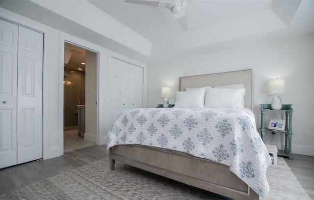 bedroom featuring dark wood-type flooring, ensuite bathroom, multiple closets, a tray ceiling, and ceiling fan