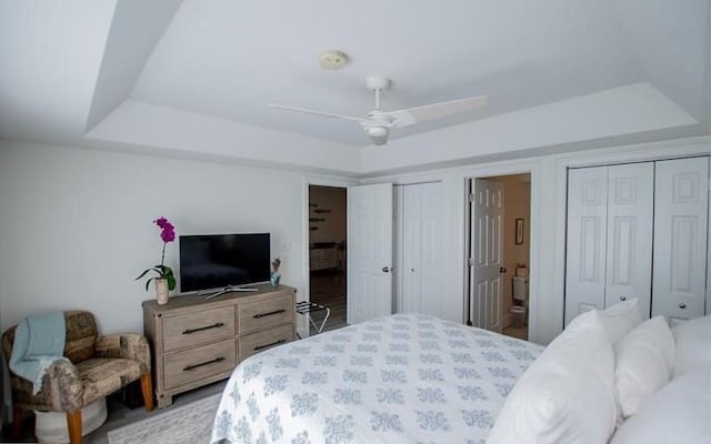 bedroom with a raised ceiling, connected bathroom, two closets, and ceiling fan