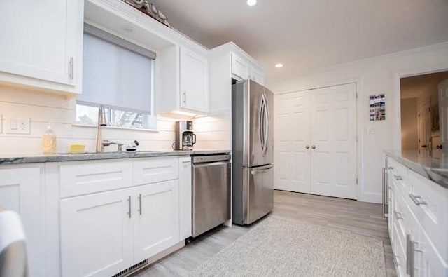 kitchen featuring sink, light wood-type flooring, appliances with stainless steel finishes, decorative backsplash, and white cabinets