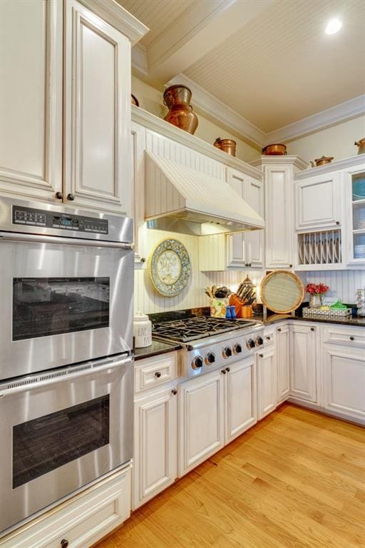 kitchen with white cabinetry, stainless steel appliances, crown molding, light wood-type flooring, and custom range hood