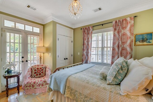 bedroom featuring french doors, an inviting chandelier, access to outside, wood-type flooring, and ornamental molding