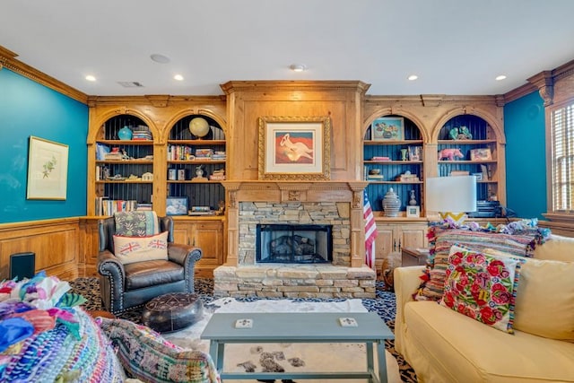 living room featuring a stone fireplace, built in shelves, and crown molding