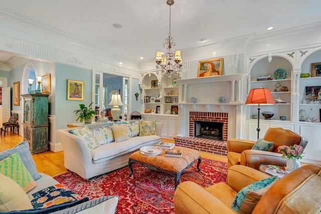 living room featuring a chandelier, built in shelves, light hardwood / wood-style floors, a fireplace, and ornamental molding