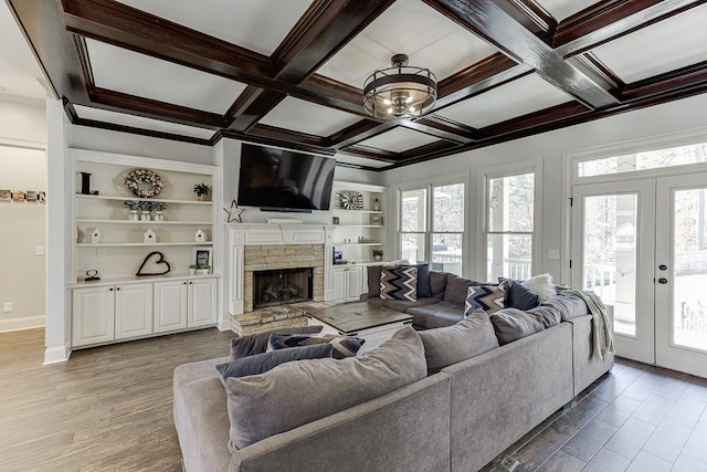 living room featuring a stone fireplace, light wood-type flooring, french doors, and coffered ceiling