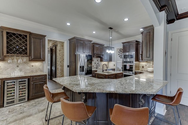 kitchen with appliances with stainless steel finishes, hanging light fixtures, a kitchen breakfast bar, a spacious island, and wine cooler