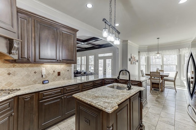 kitchen with a center island with sink, decorative light fixtures, sink, tasteful backsplash, and coffered ceiling