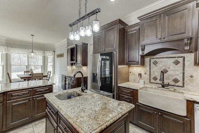 kitchen featuring light stone counters, sink, stainless steel fridge, and decorative light fixtures