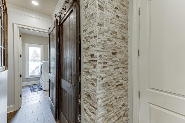 corridor with washer / clothes dryer, hardwood / wood-style flooring, crown molding, and a barn door