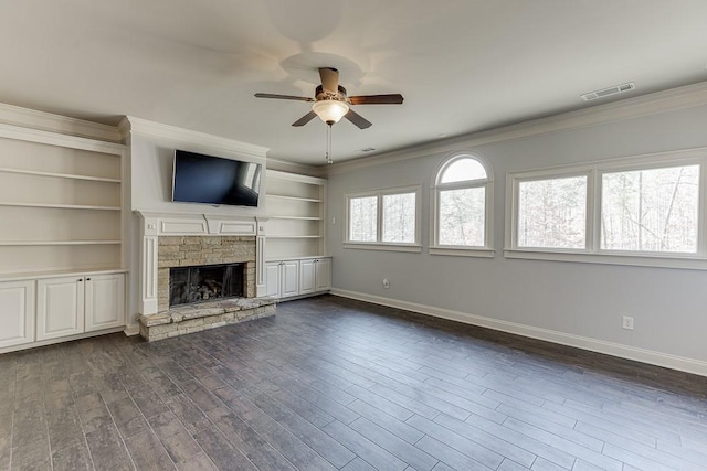 unfurnished living room featuring dark hardwood / wood-style flooring, ornamental molding, a stone fireplace, and ceiling fan