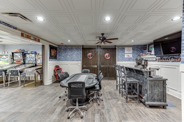 dining room featuring bar, light hardwood / wood-style flooring, ceiling fan, and a barn door