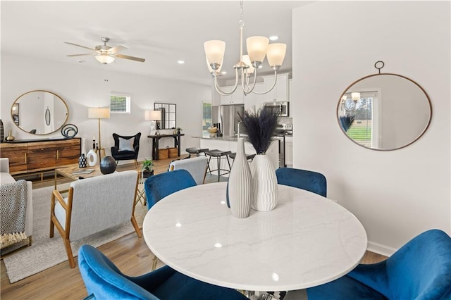 dining area with ceiling fan with notable chandelier and light hardwood / wood-style flooring