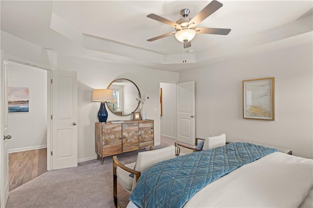 carpeted bedroom featuring ceiling fan and a tray ceiling