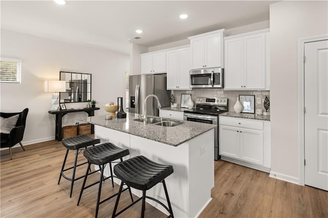 kitchen with sink, stainless steel appliances, a kitchen breakfast bar, white cabinets, and a center island with sink