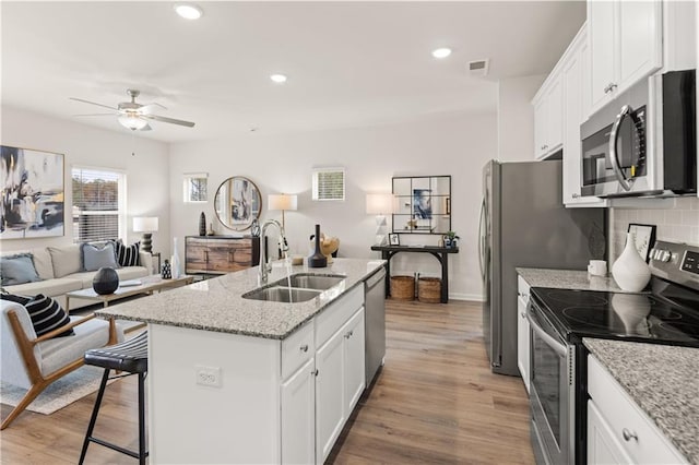 kitchen featuring sink, white cabinetry, appliances with stainless steel finishes, a kitchen breakfast bar, and an island with sink