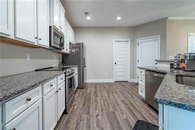 kitchen with sink, stainless steel appliances, dark stone countertops, white cabinets, and hardwood / wood-style flooring