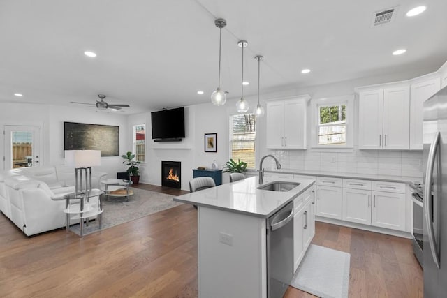 kitchen with visible vents, a sink, a warm lit fireplace, open floor plan, and stainless steel appliances