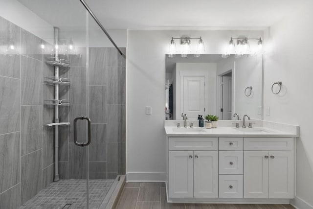 full bathroom with a sink, baseboards, double vanity, and a shower stall