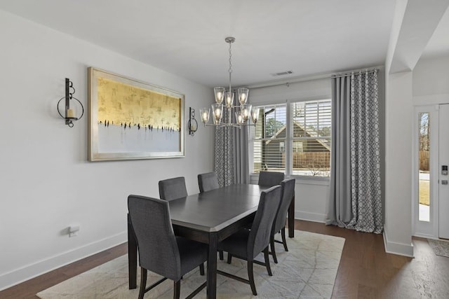 dining area featuring wood finished floors, a notable chandelier, baseboards, and visible vents