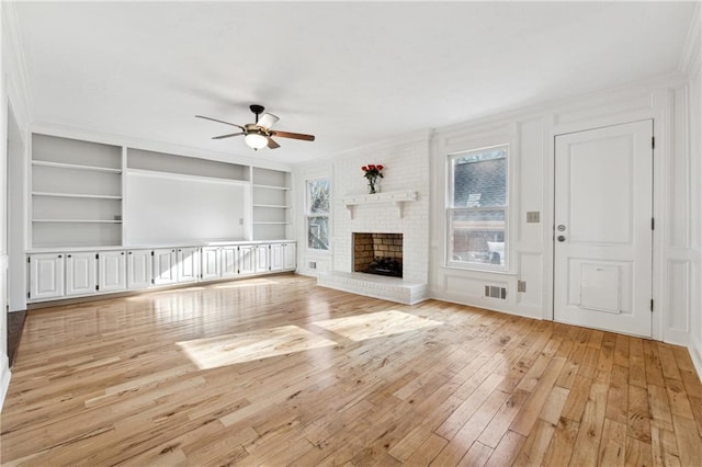 unfurnished living room featuring crown molding, built in features, ceiling fan, a fireplace, and light wood-type flooring